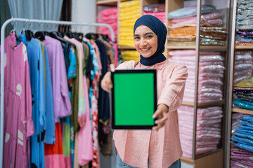 woman with hijab showing her blank screen to camera while working at her fashion warehouse. online seller