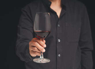 Close-up of hand holding a red wine glass while standing on a black background