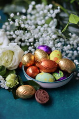 Obraz premium Foil wrapped Easter chocolate eggs in a glass bowl. Easter celebration concept. Colorful still life with sweets. Textured background with copy space. Easter greeting card. 