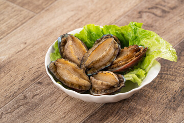 Delicious raw abalone in a plate on wooden table background.