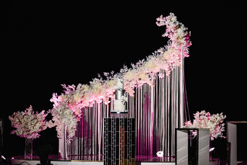 Wedding arch decorated with flowers in nature for the ceremony on pier. Cake in magical evening zone. Party. Night ceremony with light.