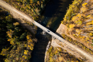 SUV on wooden bridge over small mountain river. Autumn forest.