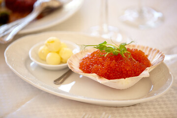 Red caviar in a clam shell on a white plate. Salmon caviar. Buffet appetizer. Table setting in a restaurant