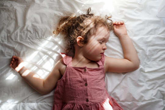 Cute little girl sleeping on bed with sunlights at home