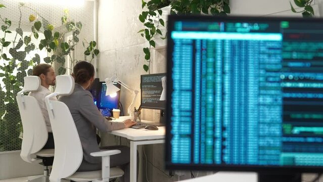 Computer monitor with large database code in modern office of successful IT company with professional female and male programmers working on computers coding. Colleagues concept.