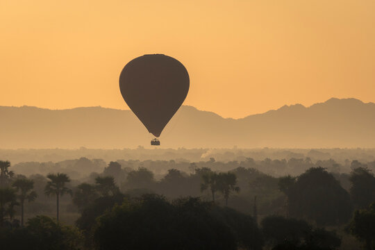 Hot-air balloon at sunrise against mountains, Bagan (Pagan)