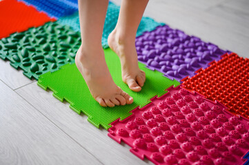 The child is engaged in orthopedic massage mats for legs of different hardness and texture. Massage of the nerve endings of the legs, prevention of flat feet in children. Treatment of foot deformity.