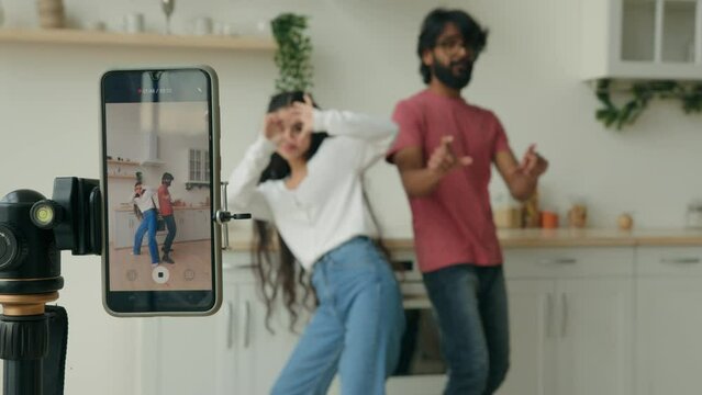 Funny couple dancing to popular music having fun in kitchen recording self video dance on mobile phone camera for social media multiracial indian arabian man woman dancers bloggers record trend move
