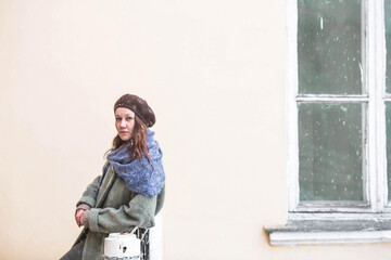 Portrait of a cute young woman in a beret in early spring outdoors . A girl with loose hair and a long coat on the background of an old manor.