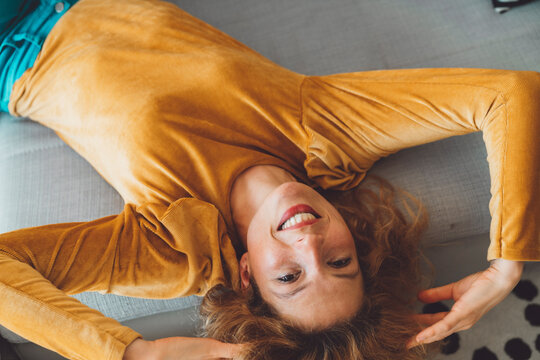 Smiling Woman Laying On The Couch In A Velvet Yellow Shirt Playing With Her Hair Looking At The Camera 