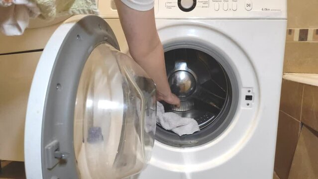 The woman is going to wash things. Close-up woman's hand opens the washing machine door, puts dirty clothes in the wash, closes the washing machine door