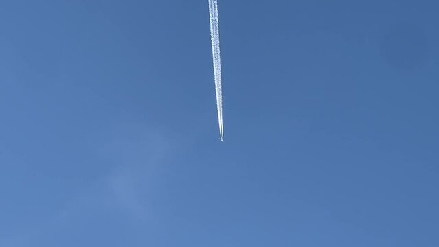 Airplane flying over heard with white contrail trailing it with a blue sky.
