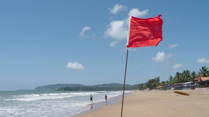 Red flag as warning sign on the beach before storm means no swimming, during windy sunny day	