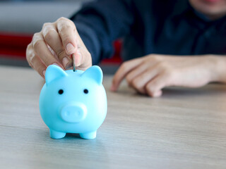 Obraz na płótnie Canvas Hand man collecting coins in blue piggy bank on desk, finance savings or investment for the future concept.