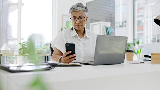 Business woman, phone and laptop at desk in office for planning, online management and administration. Mature female working on smartphone, computer and technology of multitasking on media connection