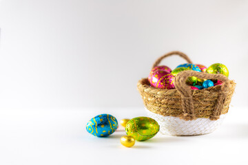 Easter eggs in basket with white background on white table. Studio lighting colorful easter decorated eggs for egg hunt with wicker basket and flowers. Banner for web and composition. Wishes card