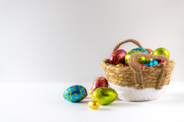 Easter eggs in basket with white background on white table. Studio lighting colorful easter decorated eggs for egg hunt with wicker basket and flowers. Banner for web and composition. Wishes card