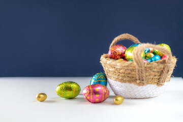 Easter eggs in basket with blue background on white table. Studio lighting colorful easter decorated eggs for egg hunt with wicker basket and flowers. Banner for web and composition. Wishes card