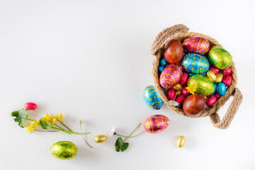 Easter eggs in basket with white background on white table. Studio lighting colorful easter decorated eggs for egg hunt with wicker basket and flowers. Banner for web and composition. Top view