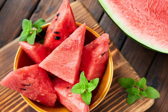 Sliced watermelon decorated with mint leaves on brown wooden background. Close-up, selective focus