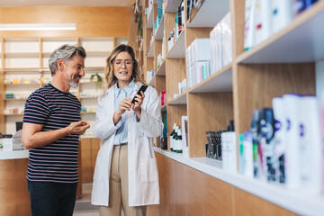 Pharmacist showing a man a skincare product in a chemist