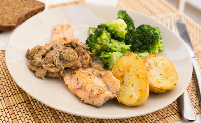 fried river trout fillet with a complex side dish of broccoli, baked potatoes and mushroom sauce