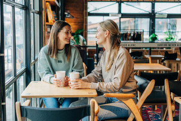 Two female friends are chatting and drinking coffee while sitting in a coffee shop.