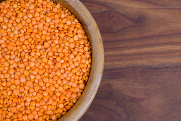 Red lentils in a wooden bowl on a wooden table.