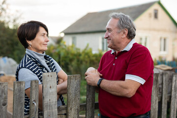 Neighbors standing at fence outdoors and having conversation. Village residents talking