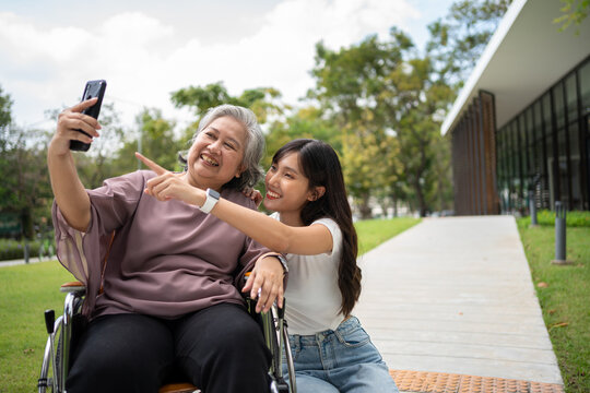 Happy Asian patients in a wheelchair use smartphones to take pictures with careful caregivers or nurse Concept of happy retirement with care from a caregiver and Savings and senior health insurance.