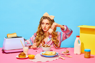 Food pop art photography. Sad young girl with long curly hair preparing milk flakes with hungry eyes over light blue background. Table with milk, butter, bread