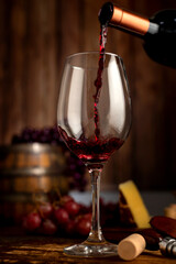red wine glass with bottle serving wine on still life table with wooden barrel grapes and cheese on wooden boards