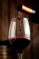red wine glass with bottle serving wine on still life table with wooden barrel grapes and cheese on...