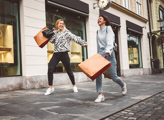 Couple of female friends shopping in the city, walking around with paper shopping bags 