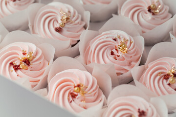 Set of cupcakes with pink whipped cream top decorated with edible golden petals and red dried berries. Close-up shot of cupcakes in the white background. Macro shot