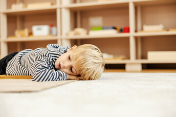 A little boy is taking a break and lying down on the floor in kindergarten.