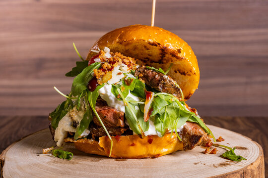 Panino da pub con tagliata di carne di bufalo, rucola fresca, burrata e cipolla croccante poggiato su un tagliere di legno e servito in una braceria