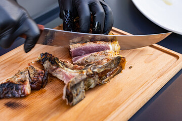 Chef di una braceria mentre scaloppa, su un tagliere di legno, con un coltello una costata di carne cotta al sangue 
