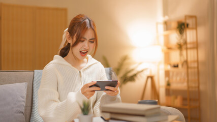 Fototapeta na wymiar Home lifestyle concept, Young woman playing game on smartphone with excited in night time at winter