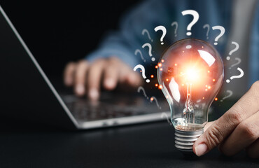 Businessman holding glowing light bulb with question icon. Find answers online. FAQ search for...