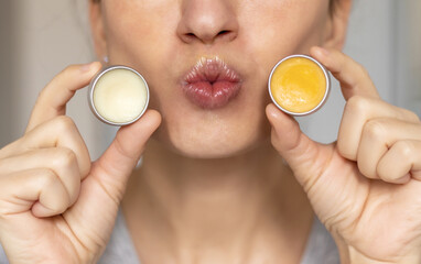 woman applying on lips balm or scrub from natural ingredients half bottom face kissing gesture smiling female.scrub and lip balm from small jars girl taking with finger rotation moves coconut oil - obrazy, fototapety, plakaty