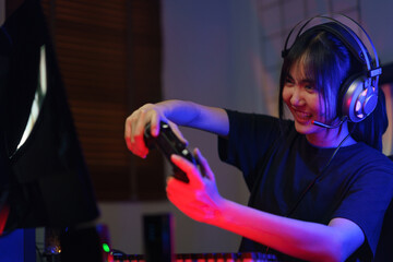 Female cyber hacker gamer in headphone playing video games on computer with joystick in neon light