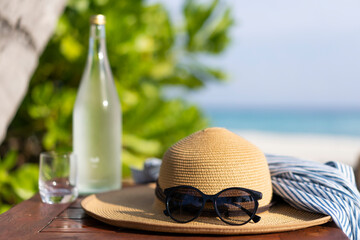 Glass bottle of water, straw hat and sun glasses on the background of the beach in the Maldives