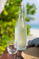 Glass bottle of water, straw hat and sun glasses on the background of the beach in the Maldives