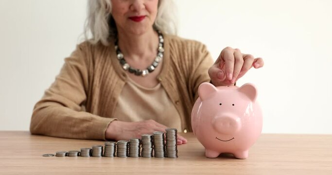 Elderly woman throwing coins into piggy bank near piles of kopecks in ascending order closeup 4k movie slow motion