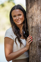Image of a beautiful happy woman posing next to a tree by the lake