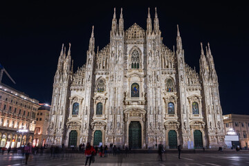 Fototapeta na wymiar Milan, Italy low angle wide shot of illuminated gothic style Roman Catholic Duomo Cathedral facade at the homonym main square.