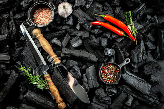 BBQ grill coal texture with fresh herbs, spices and kitchen utensils, cooking background, place for text, top view