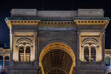 Obraz premium Milan, Italy low angle night shot of illuminated Galleria Vittorio Emanuele II entrance detail with relevant inscription, a 19th-century arcade with shops at Duomo main square.