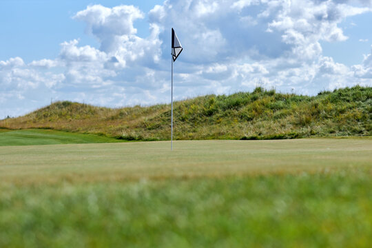 Background image of green golf field with flagstick marking hole, copy space